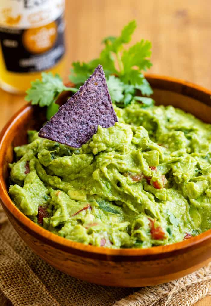 Wooden bowl filled with Guacamole with a black tortilla chip in the middle.