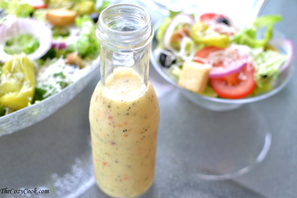 bottle of copycat olive garden salad dressing on a glass table with olive garden salad in the background.