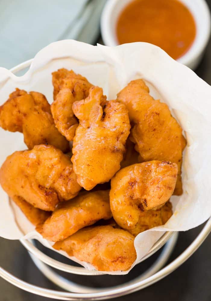 Golden fried Chinese Chicken Fingers in a serving bowl with sweet and sour sauce in the background.