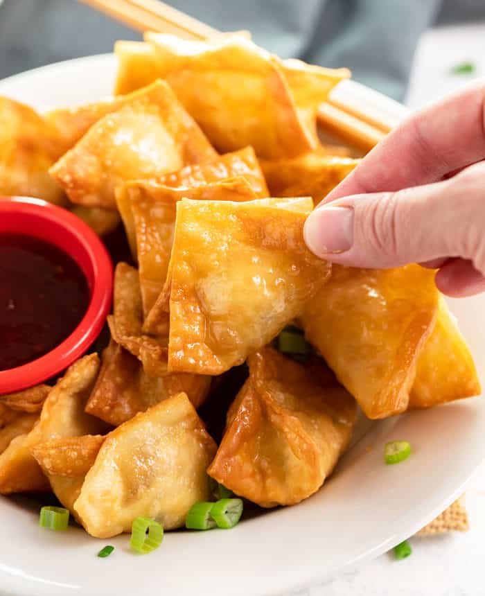 A close up shot of a hand holding fried crab rangoon. 