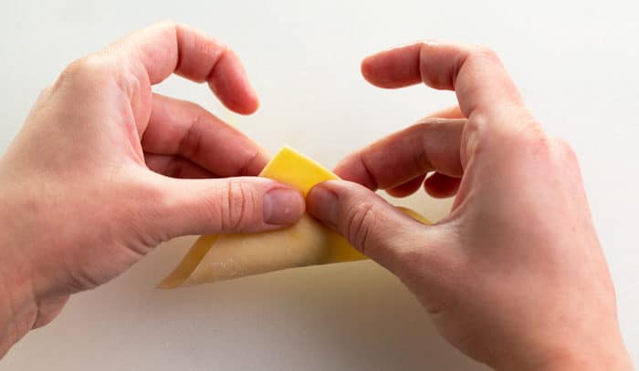 Hands folding a wonton wrapper in half to form a triangle