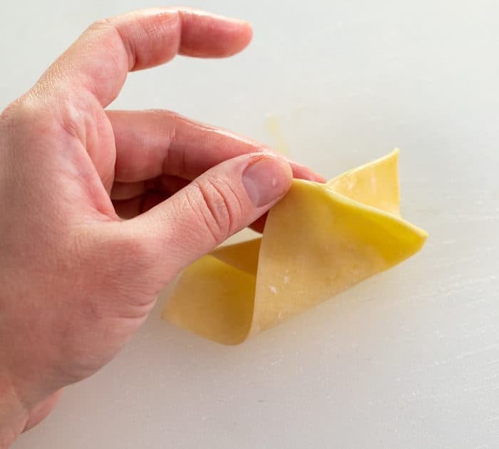 hand holding half folded wonton wrapper for crab rangoon