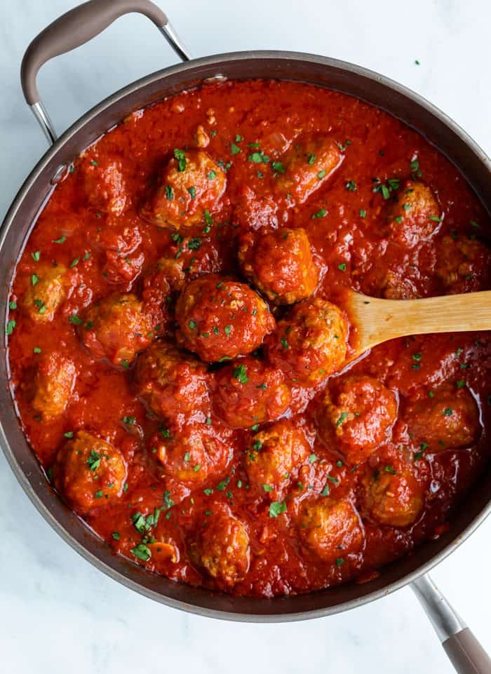 Meatballs in a homemade marinara sauce in a large pot with a wooden spoon.