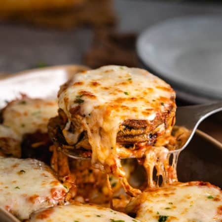 A stack of eggplant Parmesan topped with melted Mozzarella cheese being scooped up with a spatula.