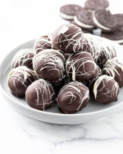 A white dessert stand with a stack of Oreo Truffles on top and Oreo Cookies in the background.