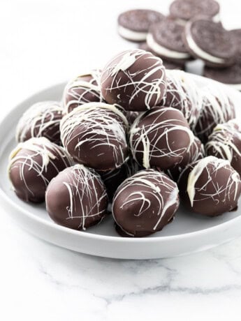 A white dessert stand with a stack of Oreo Truffles on top and Oreo Cookies in the background.