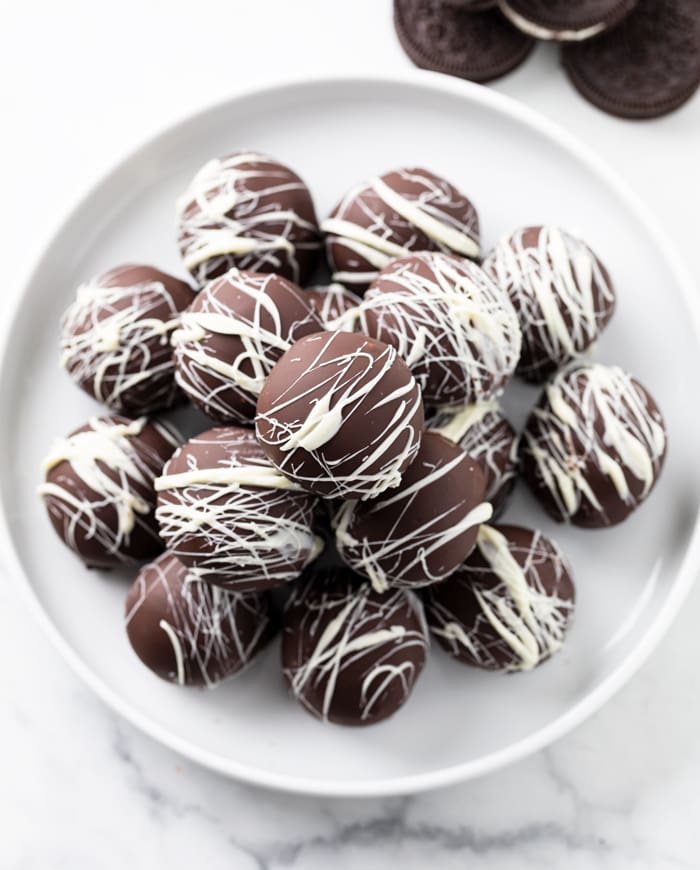 A pile of Oreo Truffles on top of a white plate with white chocolate drizzled on top.