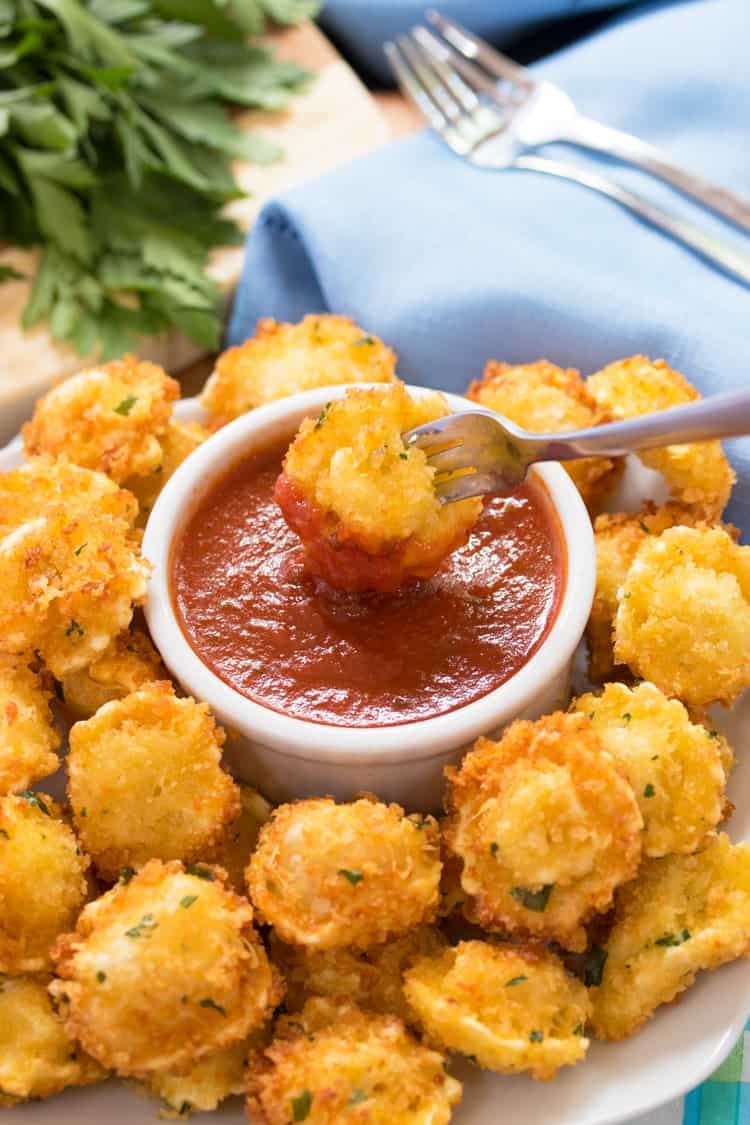 a fork dipping a fried and breaded tortellini bite into marinara sauce