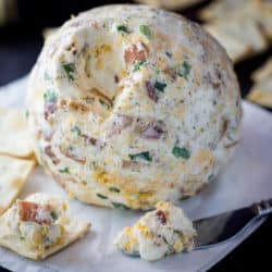 A bacon ranch cheese ball with crackers around it.