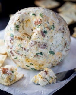 A bacon ranch cheese ball with crackers around it.