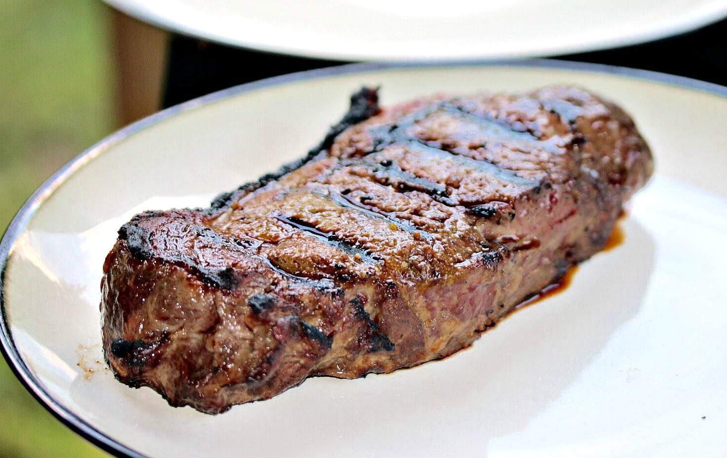 A grilled steak resting on a white plate after being cooked.