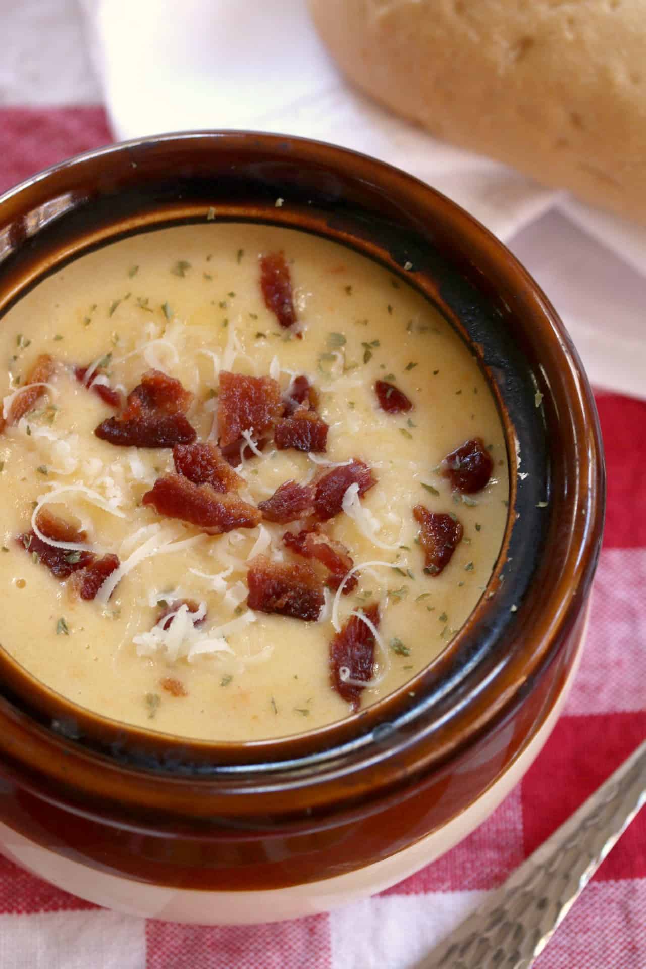 A bowl of Asiago bisque topped with crumbled bacon, parsley, and shredded cheese.