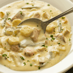 A white bowl full of creamy chicken stew topped with a spoon scooping it up.