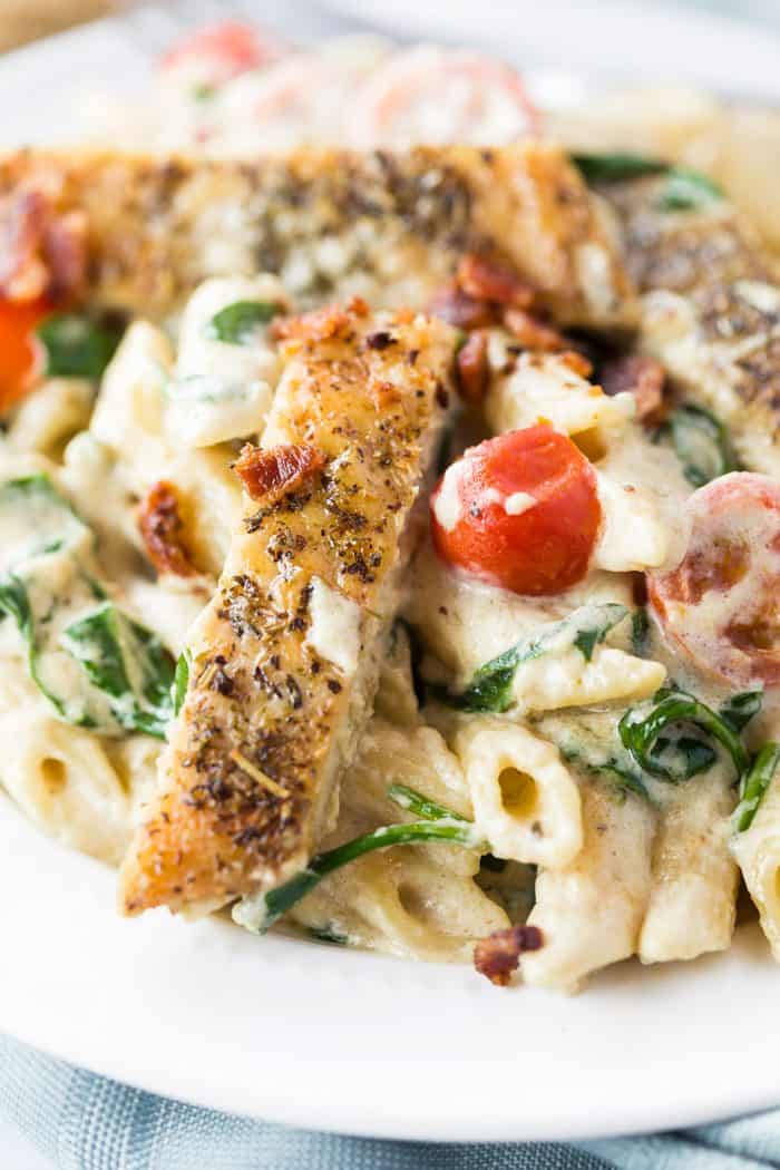 Close up image of seasoned and seared chicken next to a cherry tomato over pasta.