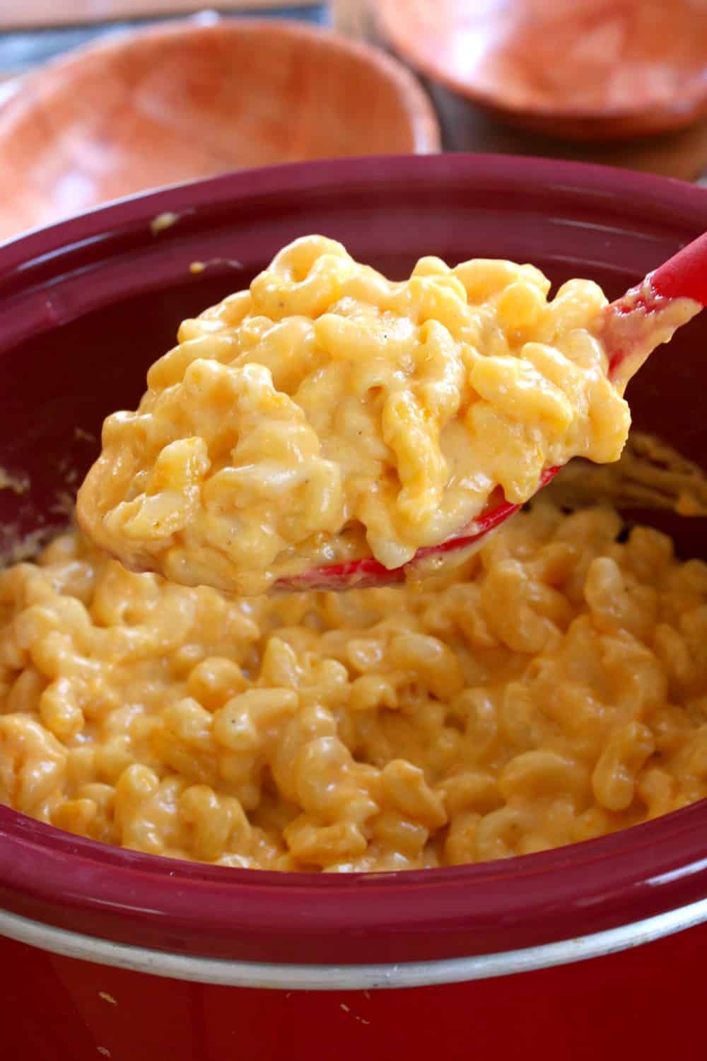 Large spoon full of macaroni and cheese scooped up from a red crock pot.