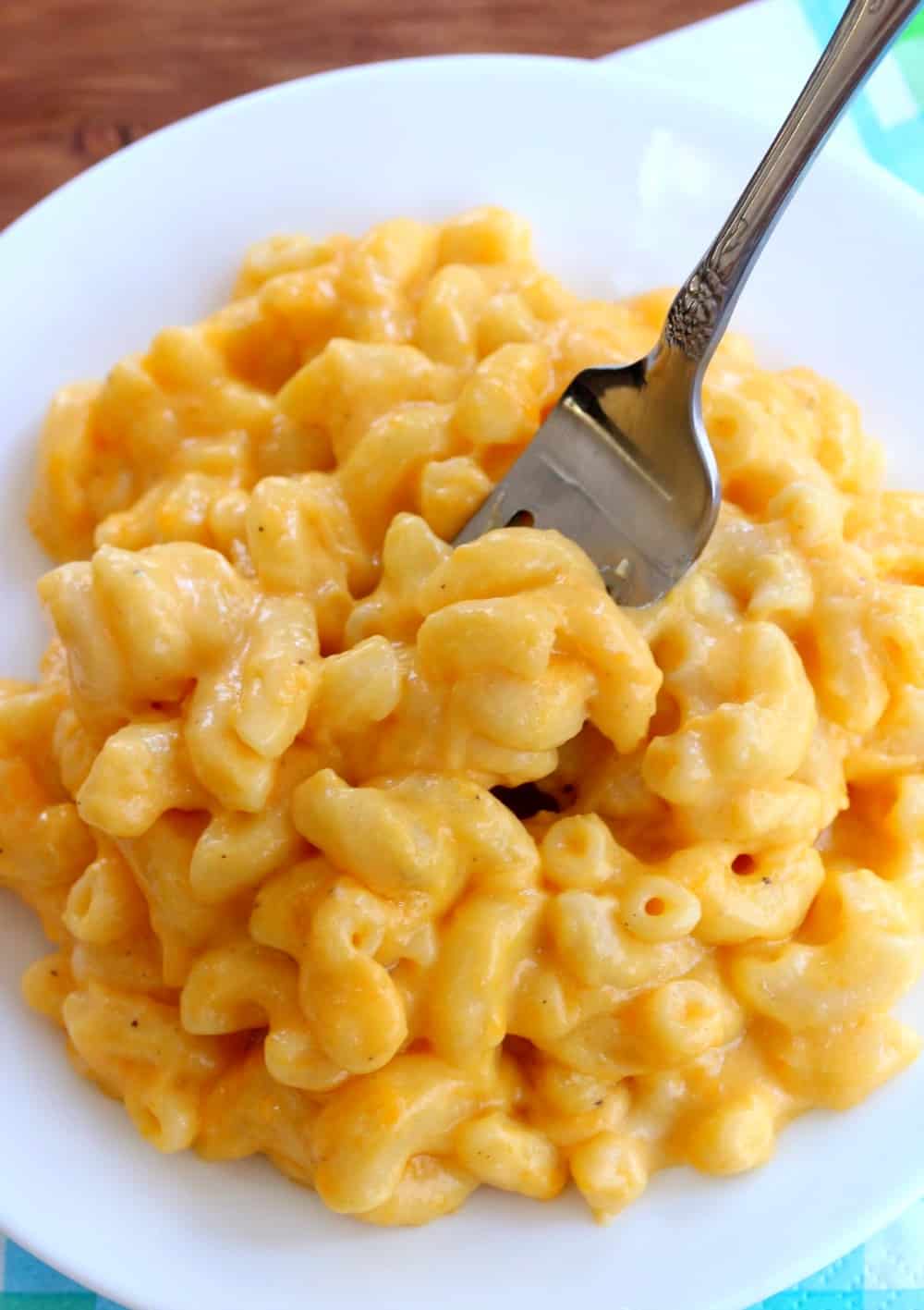 White plate full of macaroni and cheese with fork inserted into it. 