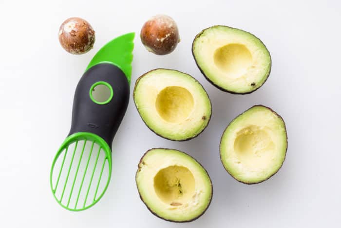 Sliced avocados with their pits removed on a white surface next to an avocado slicer.