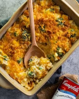 A casserole dish filled with broccoli chicken rice casserole with a can of cream of chicken soup next to it.