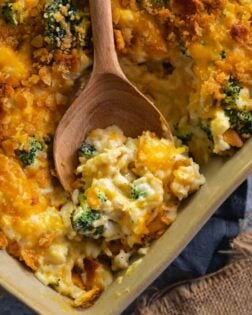 broccoli chicken rice casserole in a casserole dish with a wooden spoon scooping it up.