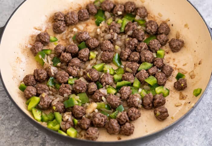 Cooked ground beef rolled into balls in a pan with onions, peppers, and garlic.