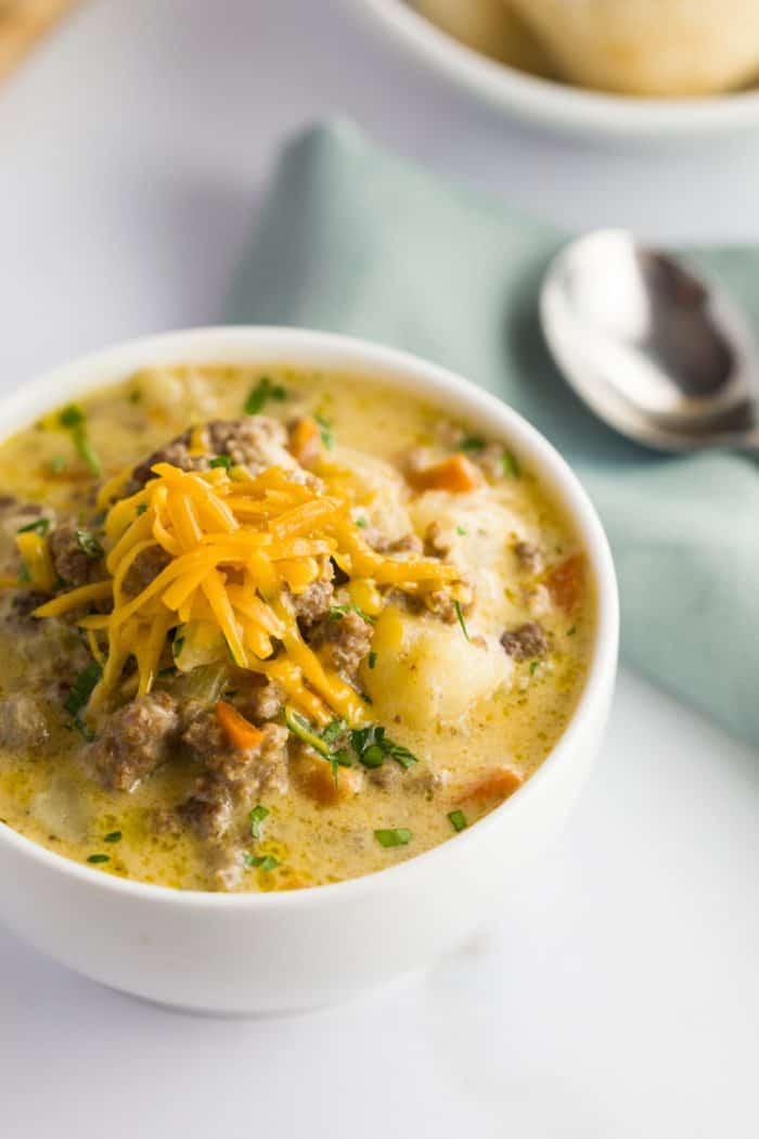 Overhead view of Cheeseburger Soup topped with grated cheese on a white table.