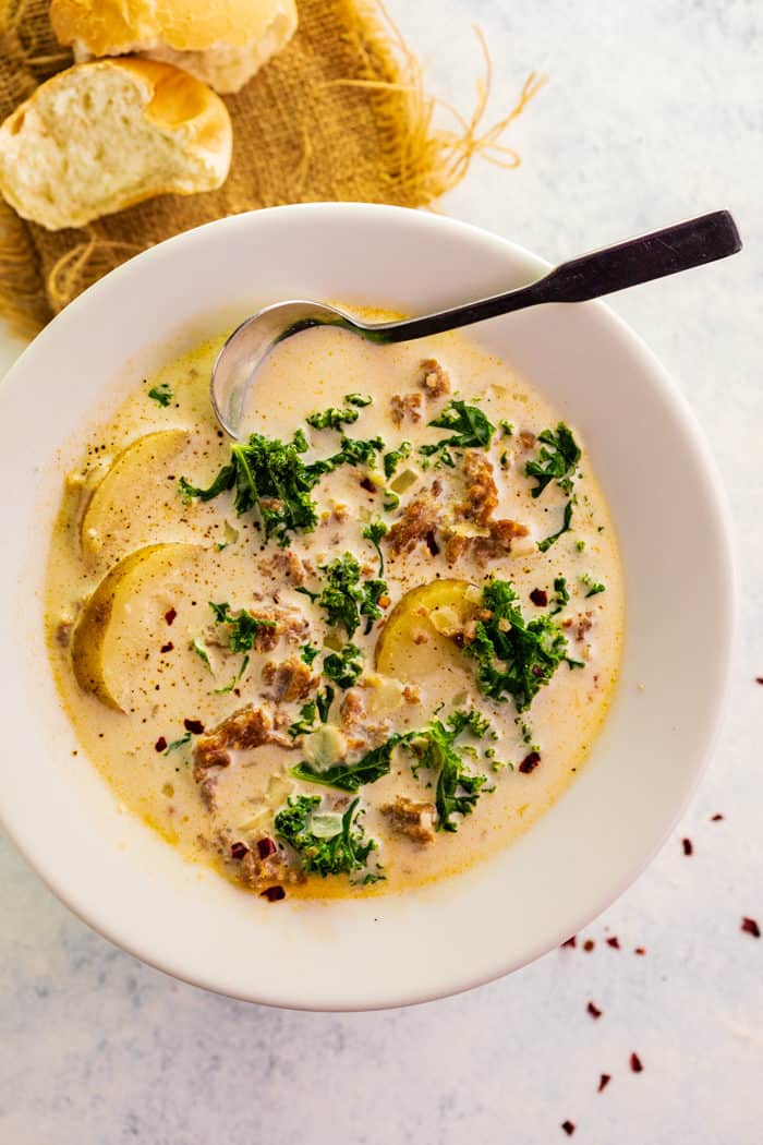 A white bowl filled with Zuppa Toscana Soup with creamy broth with potatoes, kale, and sausage. 