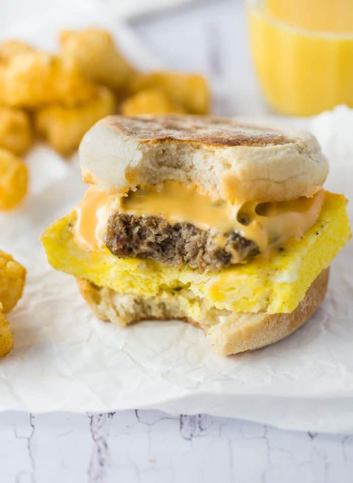 A sausage egg and cheese Breakfast Sandwiches with a bite taken out of it and tater tots in the background.