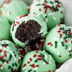 Green Oreo Truffles with sprinkles on top in a bowl, one has a bite taken from it.
