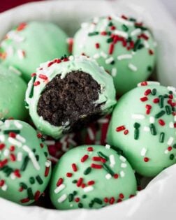 Green Oreo Truffles with sprinkles on top in a bowl, one has a bite taken from it.