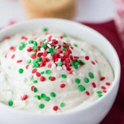 A white bowl of Christmas cookie dip with red and green sprinkles on top.