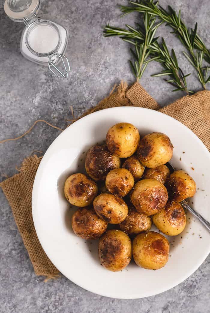 A white plate with roasted potatoes from the instant pot with fresh rosemary and sea salt.