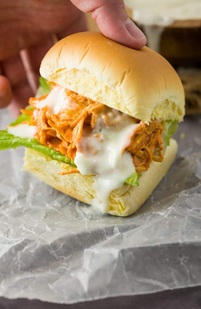 A hand grabbing a slider bun filled with sriracha chicken drizzled with blue cheese.