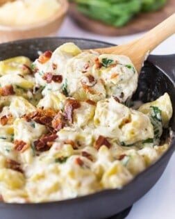 A spoon scooping out tortellini al forno from a black cast iron skillet.