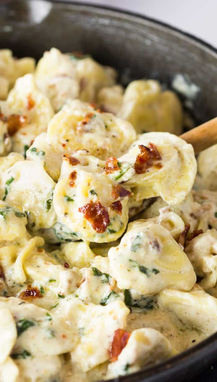 A cast iron skillet filled with tortellini in a cream sauce with bacon sprinkled on top.
