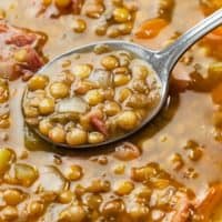 A close up view of a spoon filled with lentil soup with ham.