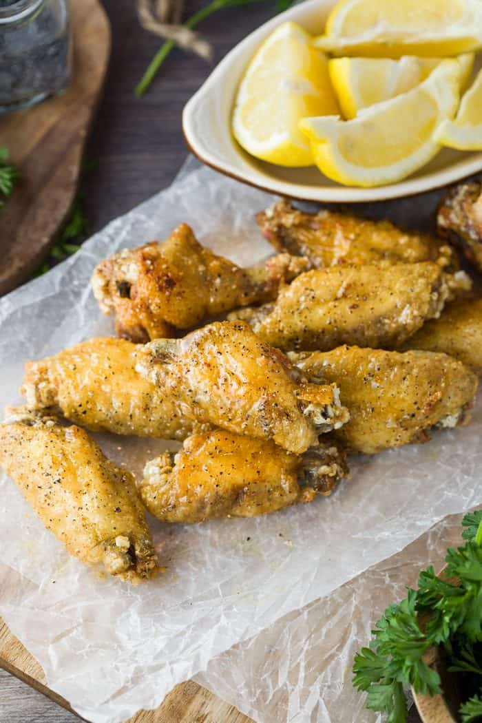 Fried chicken wings on white wax paper with lemons in the background.