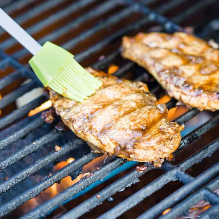 Chicken on the grill being brushed with marinade.