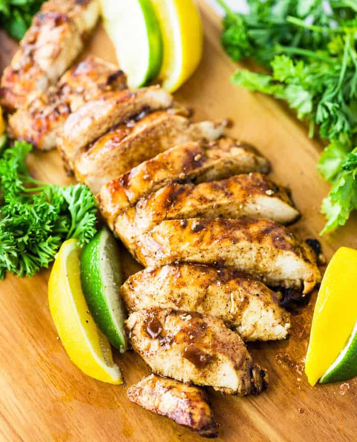 Cooked chicken sliced up on a cutting board drizzled with marinade and surrounded by lemon and lime slices with parsley.