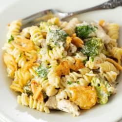 A white plate with cheesy chicken noodle casserole with broccoli and a fork in the background.