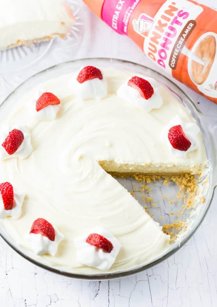 No Bake Vanilla Cheesecake in a glass pie pan with a slice cut out of it.