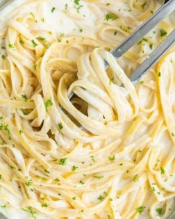 Overhead view of a pan filled with Creamy Fettuccine Alfredo with kitchen tongs.