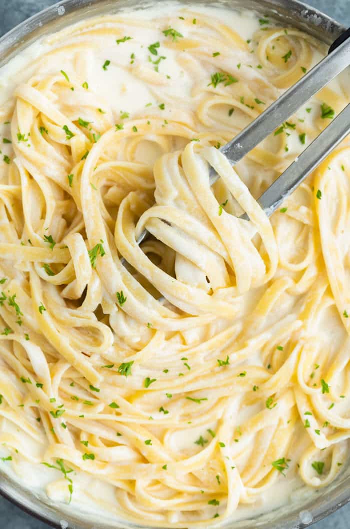 Overhead view of a skillet full of Fettuccine Alfredo with kitchen tongs in the middle.