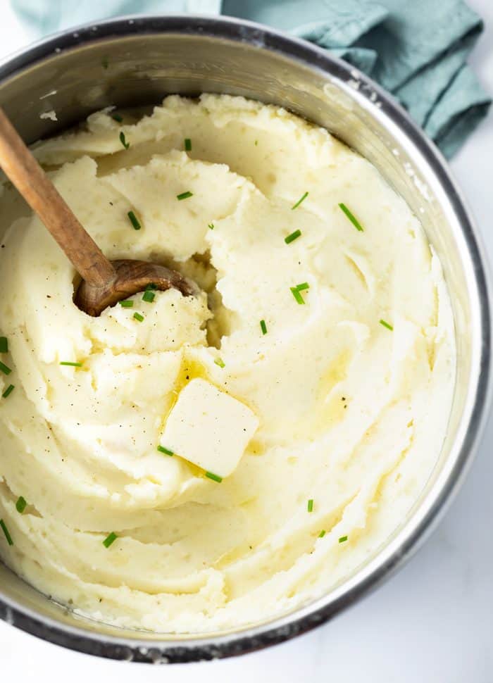 Instant Pot Filled with Mashed Potatoes topped with butter with a wooden spoon.