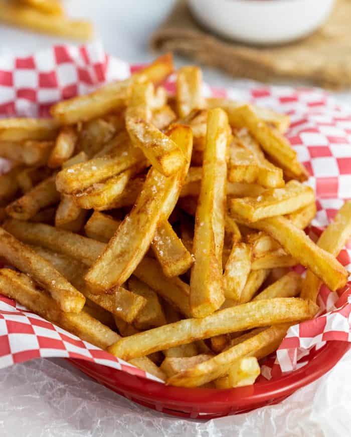 A pile of crispy, golden brown french fries in a basket sprinkled with salt. 