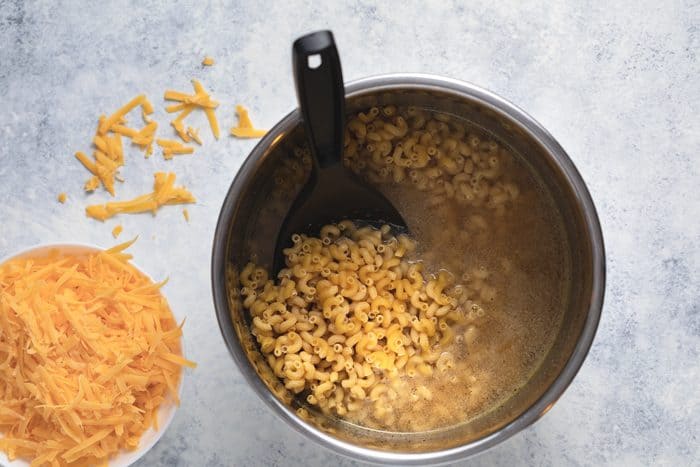 Macaroni in the Instant Pot next to a bowl of shredded cheese.