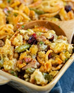 A casserole dish with a wooden spoon scooping out stuffing casserole with green beans.