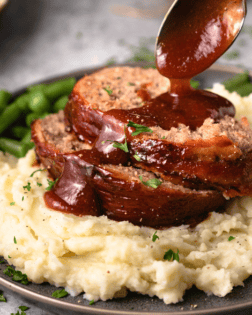 A pile of mashed potatoes with The Pioneer Woman Meatloaf with a spoon drizzling glaze on top.