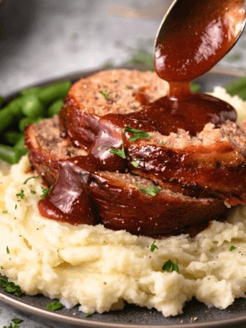 A pile of mashed potatoes with The Pioneer Woman Meatloaf with a spoon drizzling glaze on top.