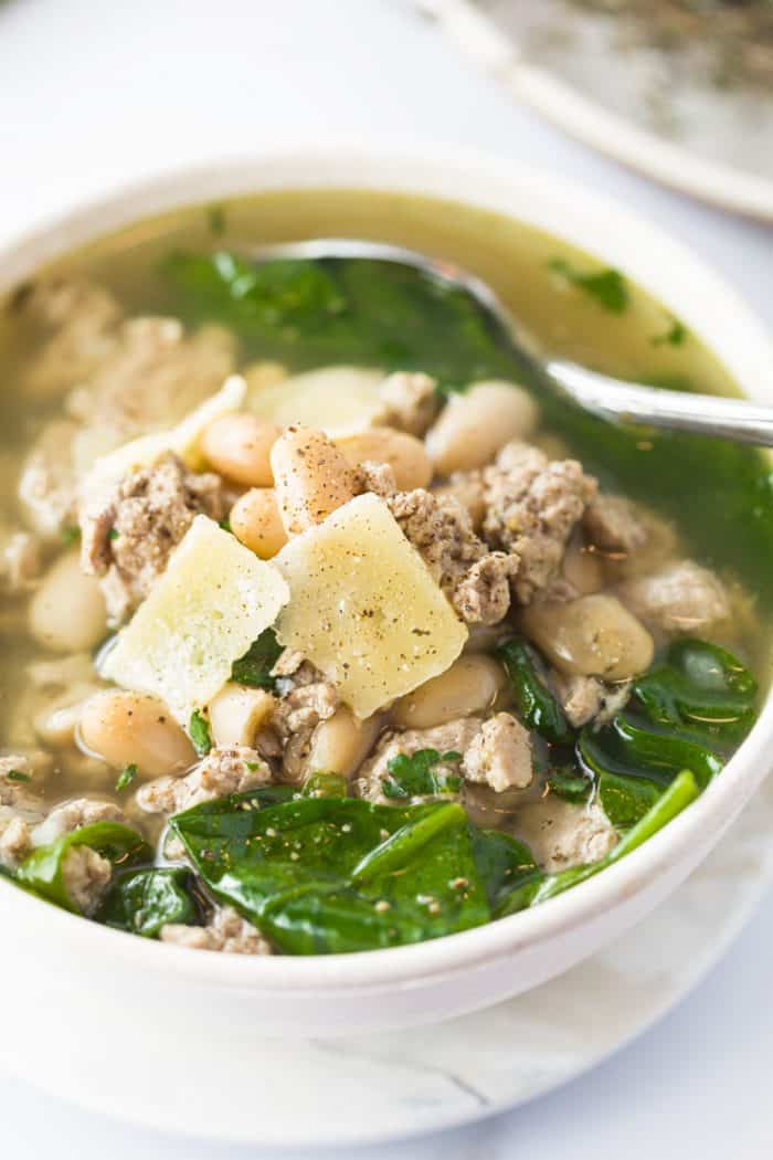 Ground Turkey, Spinach, and White Bean Soup in white bowl with Parmesan flakes on top with ground pepper.