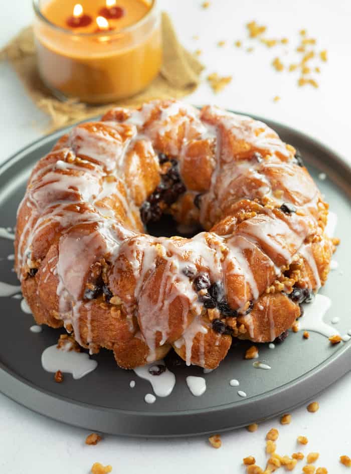 Big ring of Cinnamon Raisin Monkey Bread drizzled with white glaze on top of round baking sheet with candle in background